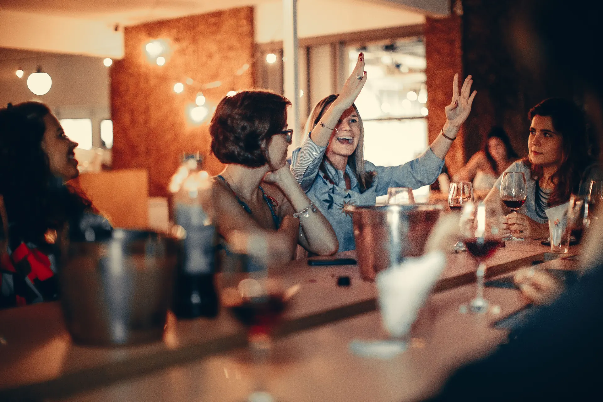 Amigas rindo em torno de uma mesa de bar com taças